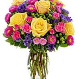 Yellow roses with pink spray roses and purple flowers in a clear glass vase