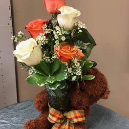 Bouquet of orange and white roses in a vase with a teddy bear