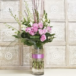 Pink roses and white snapdragons in a tall glass vase with a pink ribbon