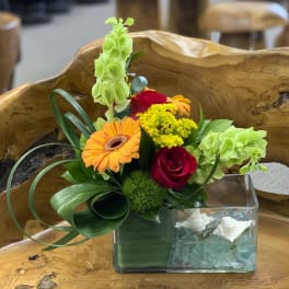 Mixed flower arrangement in a clear rectangular vase with orange and red blooms