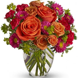 Orange roses and magenta daisies in a clear glass vase