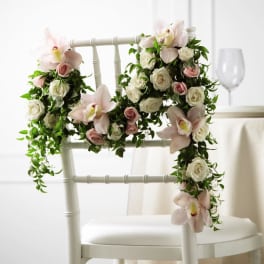 Garland of white and blush flowers draped over a white chair for event seating décor