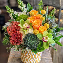 Mixed floral arrangement in a patterned yellow vase with orange roses and green orchids