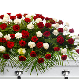 Red roses and white carnations arranged in a casket spray on a white casket