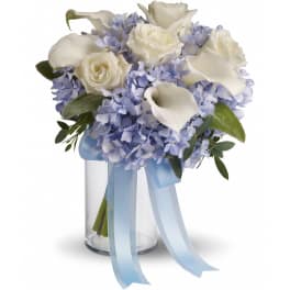 White roses and calla lilies with light blue hydrangeas in a clear glass vase with blue ribbon