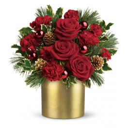 Red roses and carnations with gold pinecones in a gold vase with evergreen and holly accents.