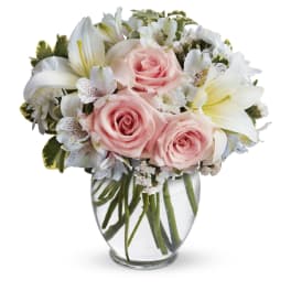 Round arrangement of pale pink roses and white lilies in a clear glass vase