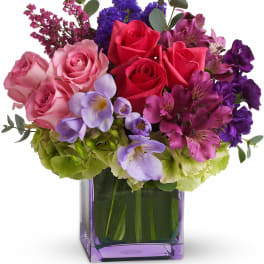 Mixed bouquet of roses, orchids, and purple blooms in a purple glass vase
