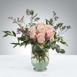 Pink roses arranged in a clear glass vase with purple filler flowers