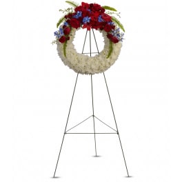 Patriotic standing wreath of white flowers with red roses and blue accents on a metal easel