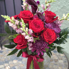 Bouquet of red roses and purple flowers in a glass vase with a ribbon