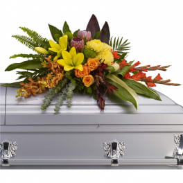 Bright tropical casket spray with yellow lilies, orange roses, orchids, and protea on a silver casket.