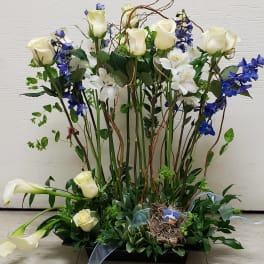Tall floral arrangement with white roses, blue flowers, and calla lilies in a black tray