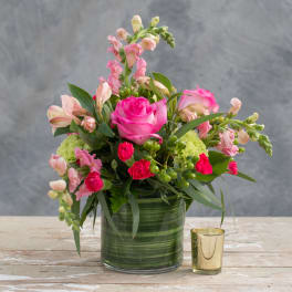 Pink roses and snapdragons arranged in a green glass vase.