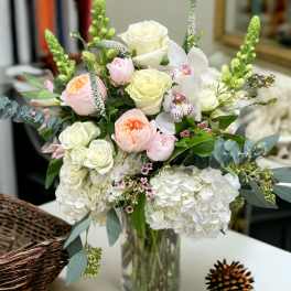 Pastel bouquet of roses, hydrangeas, and orchids arranged in a clear glass vase