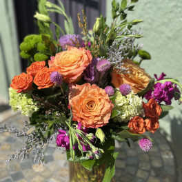 Vase arrangement of bright orange roses, green hydrangeas, and purple accent flowers.
