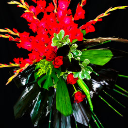 Tall red floral arrangement with tropical leaves on a black background