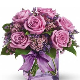 Pink roses in a purple glass vase with a ribbon bow