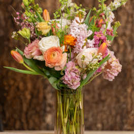 Tall mixed bouquet of pink, peach, and white flowers in a clear glass vase.