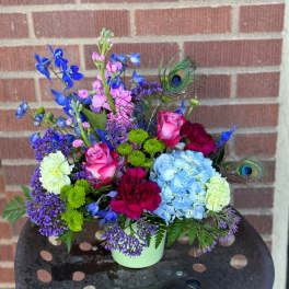 Colorful mixed bouquet in a pale green container with peacock feathers