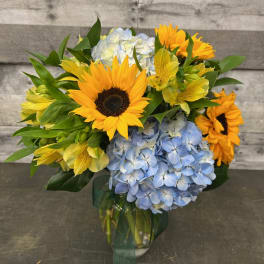 Bouquet of sunflowers, blue hydrangeas, and yellow alstroemeria in a glass vase