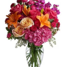 Mixed bouquet of roses, lilies, and pink blooms in a clear glass vase