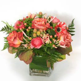 Pink and coral flower arrangement in a clear square vase