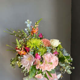 Mixed bouquet with pink, white, and green flowers in a pink container