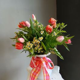 Pink and coral tulips arranged in a white vase with a plaid ribbon