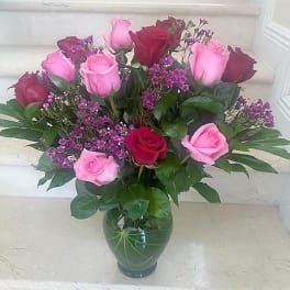 Arrangement of pink and red roses with small purple flowers in a green glass vase