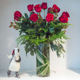 Red roses in a clear glass vase with a small penguin figurine beside it