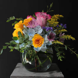 Mixed bouquet of roses, hydrangea, and purple flowers in a glass vase