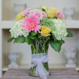 Pastel bouquet of pink gerbera, yellow roses and white hydrangeas in a clear glass vase with a ribbon bow