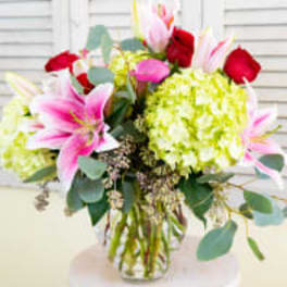 Bouquet of pink lilies, red roses, and green hydrangeas in a glass vase