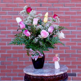 Mixed pink and white roses in a dark vase with a small figurine beside it