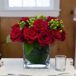 Red roses in a square glass vase with green berry accents