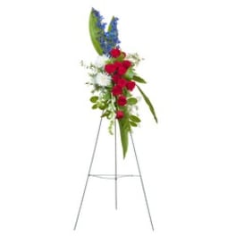 Tall floral spray with red roses, white blooms, and blue accents on a stand