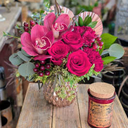 Pink roses and orchids in a glass vase beside a red candle jar