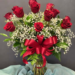 Red roses and baby's breath in a glass vase with a red ribbon