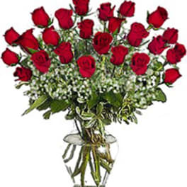 Tall arrangement of red roses with white filler flowers in a clear glass vase