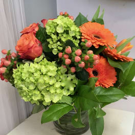 Bouquet of orange roses, green hydrangeas, and orange gerbera daisies in a glass vase
