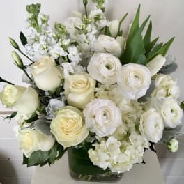 White roses and ranunculus in a glass vase with white filler flowers