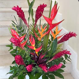 Tall tropical arrangement with red and orange flowers in a white square vase
