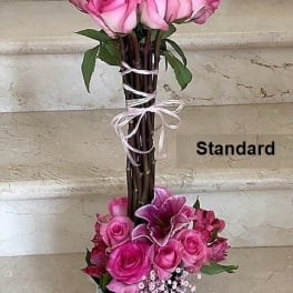 Tall arrangement of pink roses and lilies in a white square vase with bundled stems tied with ribbon