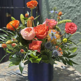 Colorful mixed bouquet in a dark blue vase with orange and pink roses