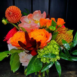 Bright mixed bouquet of orange, pink, and green flowers in a glass vase