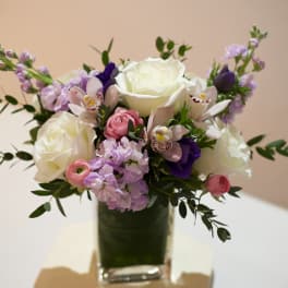 Bouquet of white roses, pink blooms, and purple flowers in a glass vase
