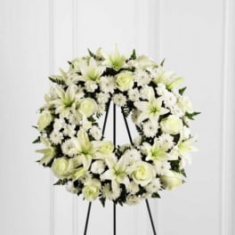 White floral wreath on a black stand with lilies and roses