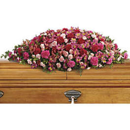 Pink and red floral casket spray on a wooden casket