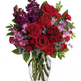 Red roses and purple flowers arranged in a clear glass vase